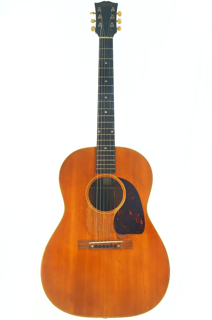Eine Gibson LG-3 Akustik Gitarre aus dem Jahr 1954 mit einem Holzkorpus, einem dunklen Griffbrett und sechs Saiten, dargestellt vor einem weißen Hintergrund. Eine Gibson LG-3 Akustik Gitarre aus dem Jahr 1954 mit einem Holzkorpus, einem dunklen Griffbrett und sechs Saiten, dargestellt vor einem weißen Hintergrund.