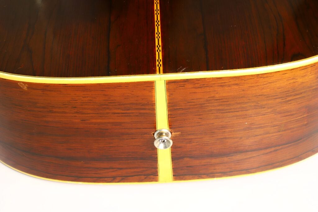 Nahaufnahme der Rückseite und der Seite der Martin D-28 Akustikgitarre aus dem Jahr 1965, bei der der Gurtknopf, die Einlage in der Mittelstreifen und die gelbe Einfassung vor der eleganten Holzmaserung besonders hervorgehoben werden. Nahaufnahme der Rückseite und der Seite der Martin D-28 Akustikgitarre aus dem Jahr 1965, bei der der Gurtknopf, die Einlage in der Mittelstreifen und die gelbe Einfassung vor der eleganten Holzmaserung besonders hervorgehoben werden.