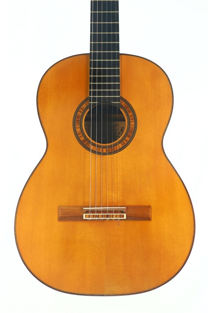 Die „Frank-Peter Dietrich 1998 Tosca Klassische Gitarre“ ist eine sechssaitige klassische Akustikgitarre mit einem Holzkorpus, einem runden Schallloch mit einer verzierten Rosette und einem dunklen Griffbrett, die auf einem Foto vor weißem Hintergrund zu sehen ist. Die „Frank-Peter Dietrich 1998 Tosca Klassische Gitarre“ ist eine sechssaitige klassische Akustikgitarre mit einem Holzkorpus, einem runden Schallloch mit einer verzierten Rosette und einem dunklen Griffbrett, die auf einem Foto vor weißem Hintergrund zu sehen ist.