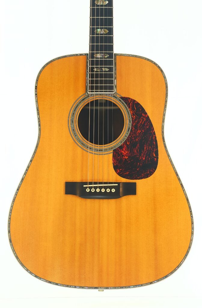 Eine Nahaufnahme des Korpus einer Akustikgitarre, die eine natürliche Holzoberfläche, ein dunkles Schildpatt-Schlagbrett, sechs Saiten und kunstvolle Einlagen auf dem Griffbrett zeigt. Eine Nahaufnahme des Korpus einer Akustikgitarre, die eine natürliche Holzoberfläche, ein dunkles Schildpatt-Schlagbrett, sechs Saiten und kunstvolle Einlagen auf dem Griffbrett zeigt.