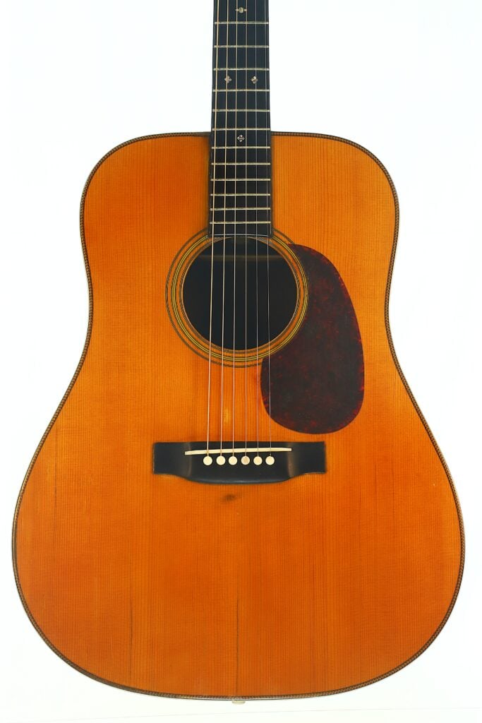 Eine Nahaufnahme der Martin D-28 1941 Pre-War Akustikgitarre, die ihre natürliche Holzoberfläche, das schwarze Schlagbrett und die sechs Saiten vor einem schlichten weißen Hintergrund zeigt. Eine Nahaufnahme der Martin D-28 1941 Pre-War Akustikgitarre, die ihre natürliche Holzoberfläche, das schwarze Schlagbrett und die sechs Saiten vor einem schlichten weißen Hintergrund zeigt.