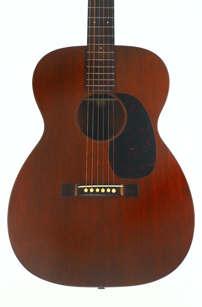 Eine Vorderansicht der Martin 00-17 Akustikgitarre aus dem Jahr 1941 mit einem dunkelbraunen Holzkorpus, sechs Saiten und einem schwarzen Schlagbrett, fotografiert vor weißem Hintergrund. Eine Vorderansicht der Martin 00-17 Akustikgitarre aus dem Jahr 1941 mit einem dunkelbraunen Holzkorpus, sechs Saiten und einem schwarzen Schlagbrett, fotografiert vor weißem Hintergrund.