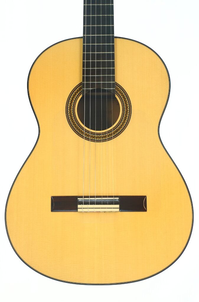 Die Lester DeVoe 2020 Negra Flamenco-Gitarre verfügt über einen Korpus aus hellem Holz, eine aufwendig gearbeitete Rosette, die das Schallloch umgibt, sechs Saiten und ein Griffbrett aus dunklem Holz, das sich vor einem weißen Hintergrund abhebt. Die Lester DeVoe 2020 Negra Flamenco-Gitarre verfügt über einen Korpus aus hellem Holz, eine aufwendig gearbeitete Rosette, die das Schallloch umgibt, sechs Saiten und ein Griffbrett aus dunklem Holz, das sich vor einem weißen Hintergrund abhebt.