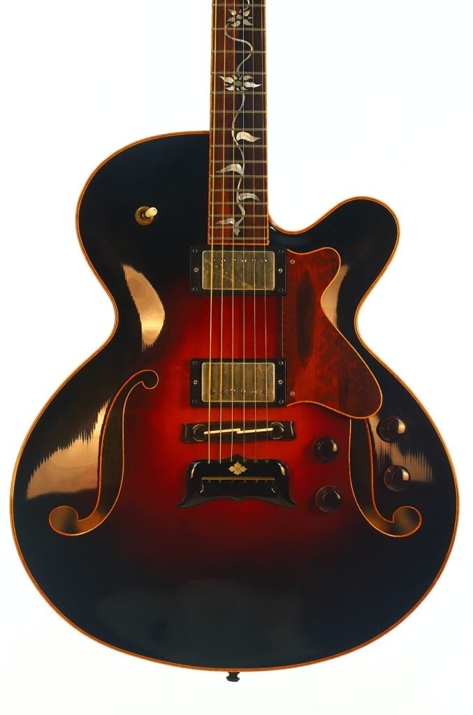 Die DeLaHaye 1995 Elektro-Akustik-Gitarre, eine halbhohle E-Gitarre im Sunburst-Design, verfügt über zwei Humbucker-Tonabnehmer, goldene Beschläge, kunstvolle Griffbrett-Einlagen, klassische F-Löcher und mehrere Regler, die vor einem weißen Hintergrund zu sehen sind. Die DeLaHaye 1995 Elektro-Akustik-Gitarre, eine halbhohle E-Gitarre im Sunburst-Design, verfügt über zwei Humbucker-Tonabnehmer, goldene Beschläge, kunstvolle Griffbrett-Einlagen, klassische F-Löcher und mehrere Regler, die vor einem weißen Hintergrund zu sehen sind.