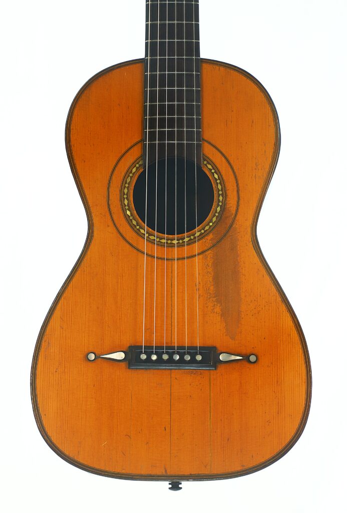 Eine Vintage-Romantikgitarre von Louis Panormo aus dem Jahr 1827 mit Holzoberfläche, sechs Saiten, einer dekorativen Rosette, die das Schallloch umgibt, sowie sichtbaren Gebrauchsspuren am Korpus. Eine Vintage-Romantikgitarre von Louis Panormo aus dem Jahr 1827 mit Holzoberfläche, sechs Saiten, einer dekorativen Rosette, die das Schallloch umgibt, sowie sichtbaren Gebrauchsspuren am Korpus.