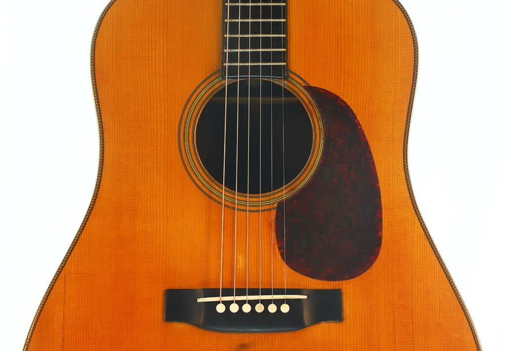 Nahaufnahme des Korpus der Martin D-28 1941 Pre-War Akustikgitarre, wobei das Schallloch, die Saiten, das Schlagbrett und der Steg vor einem weißen Hintergrund hervorgehoben sind. Nahaufnahme des Korpus der Martin D-28 1941 Pre-War Akustikgitarre, wobei das Schallloch, die Saiten, das Schlagbrett und der Steg vor einem weißen Hintergrund hervorgehoben sind.