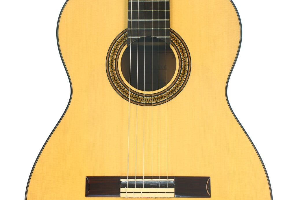 Nahaufnahme des Korpus und der Saiten einer Lester DeVoe 2020 Negra Flamenco-Gitarre, wobei das Schallloch mit seiner dekorativen Einlage und ein Teil des Halses besonders hervorgehoben sind. Nahaufnahme des Korpus und der Saiten einer Lester DeVoe 2020 Negra Flamenco-Gitarre, wobei das Schallloch mit seiner dekorativen Einlage und ein Teil des Halses besonders hervorgehoben sind.