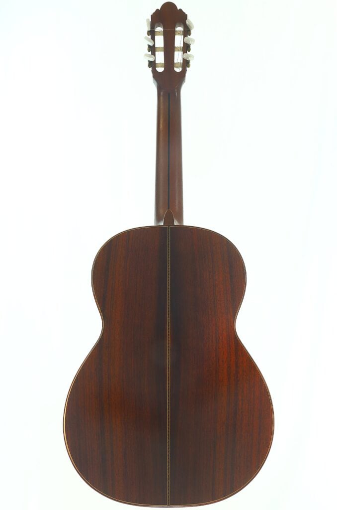 Zu sehen ist die Rückseite der „Tosca Klassische Gitarre“ von Frank-Peter Dietrich aus dem Jahr 1998 mit ihrem polierten Korpus aus dunklem Holz, dem Hals und der Kopfplatte mit den Stimmwirbeln vor einem schlichten weißen Hintergrund. Zu sehen ist die Rückseite der „Tosca Klassische Gitarre“ von Frank-Peter Dietrich aus dem Jahr 1998 mit ihrem polierten Korpus aus dunklem Holz, dem Hals und der Kopfplatte mit den Stimmwirbeln vor einem schlichten weißen Hintergrund.