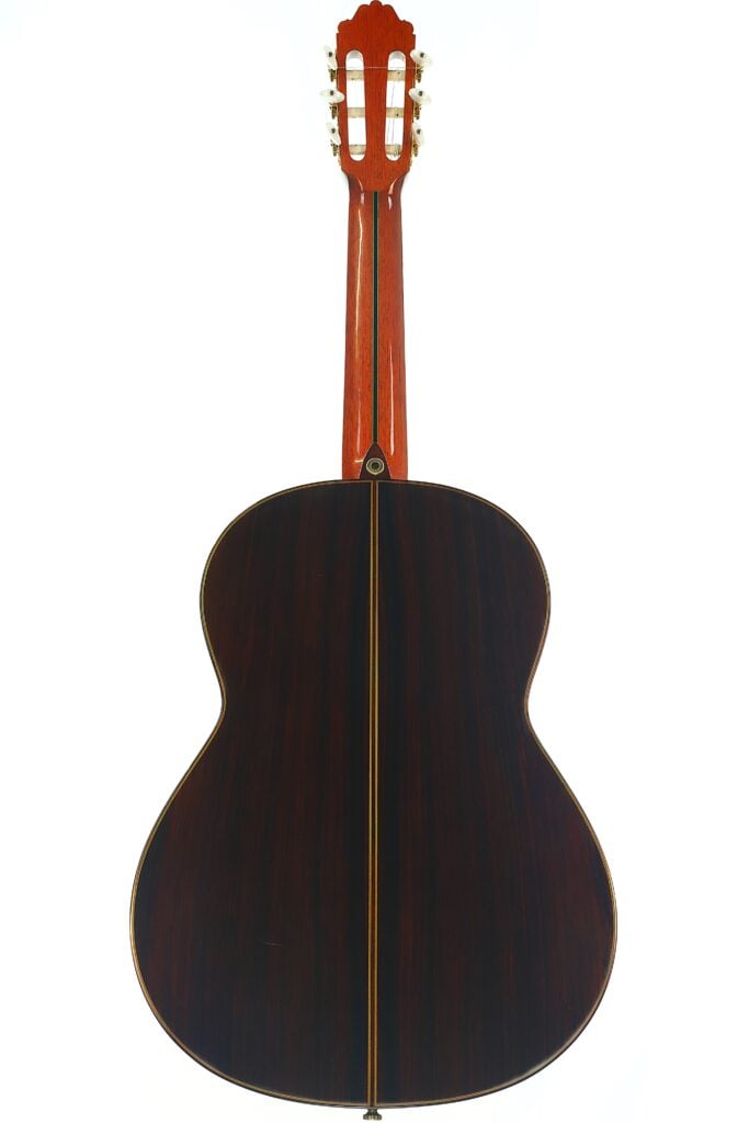 Die klassische Gitarre „Paulino Bernabe M-5 2008“ wird von hinten gezeigt und präsentiert ihren dunklen, polierten Holzkorpus mit einer hellen Mittelnaht sowie einen rötlichen Holzhals mit Stimmwirbeln – alles vor einem weißen Hintergrund. Die klassische Gitarre „Paulino Bernabe M-5 2008“ wird von hinten gezeigt und präsentiert ihren dunklen, polierten Holzkorpus mit einer hellen Mittelnaht sowie einen rötlichen Holzhals mit Stimmwirbeln – alles vor einem weißen Hintergrund.