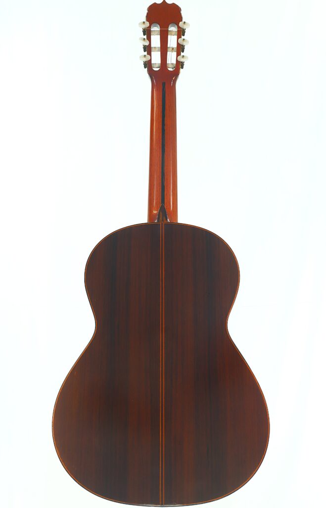Eine Ramirez 1a 1985 Klassische Gitarre, von hinten fotografiert, wobei der dunkle Holzkorpus, der mittige Einlegestreifen und der Hals mit den Stimmwirbeln vor einem schlichten weißen Hintergrund hervorgehoben werden. Eine Ramirez 1a 1985 Klassische Gitarre, von hinten fotografiert, wobei der dunkle Holzkorpus, der mittige Einlegestreifen und der Hals mit den Stimmwirbeln vor einem schlichten weißen Hintergrund hervorgehoben werden.
