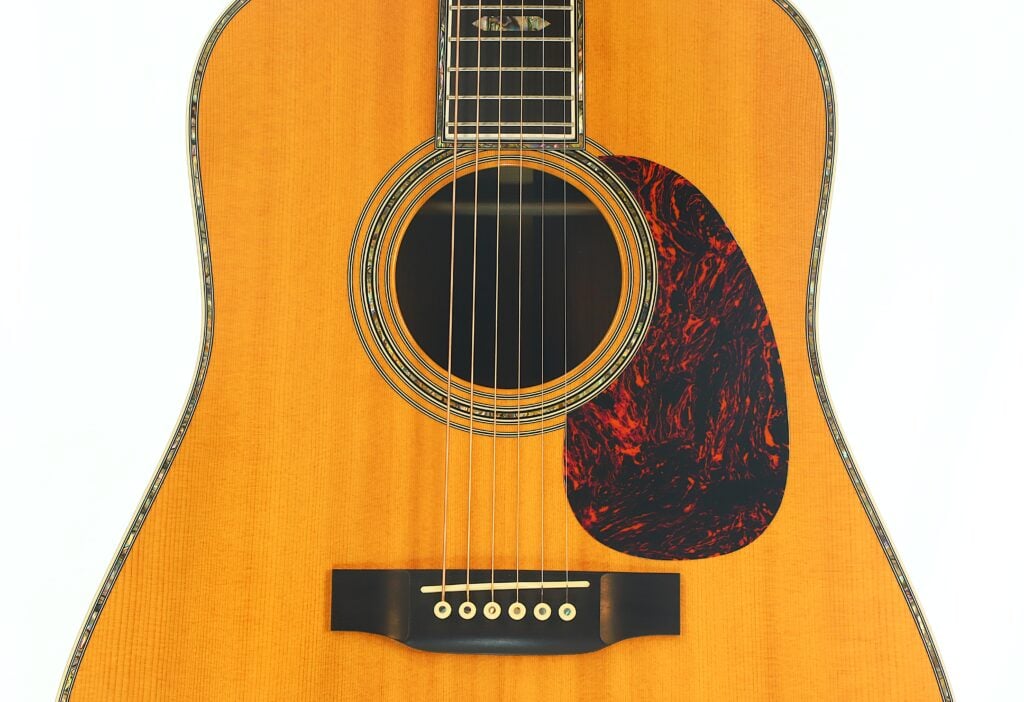 Nahaufnahme des Korpus einer Akustikgitarre, auf der das Schallloch, die Saiten, das Schlagbrett und ein Teil des Stegs vor weißem Hintergrund zu sehen sind. Nahaufnahme des Korpus einer Akustikgitarre, auf der das Schallloch, die Saiten, das Schlagbrett und ein Teil des Stegs vor weißem Hintergrund zu sehen sind.