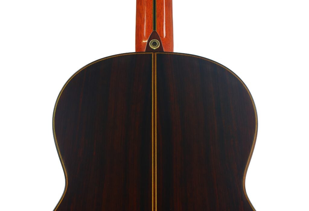 Nahaufnahme der Rückseite einer Paulino Bernabe M-5 2008 Klassische Gitarre, die dunkles Holz mit einem gelben Streifen in der Mitte und einer filigranen Maserung zeigt. Nahaufnahme der Rückseite einer Paulino Bernabe M-5 2008 Klassische Gitarre, die dunkles Holz mit einem gelben Streifen in der Mitte und einer filigranen Maserung zeigt.