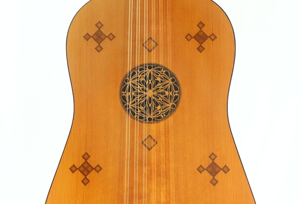 Nahaufnahme der Resonanzdecke der Vihuela von Hans Herb aus dem Jahr 1989 mit kunstvollen geometrischen Mustern und einer dekorativen Rosette um das Schallloch, vor weißem Hintergrund. Nahaufnahme der Resonanzdecke der Vihuela von Hans Herb aus dem Jahr 1989 mit kunstvollen geometrischen Mustern und einer dekorativen Rosette um das Schallloch, vor weißem Hintergrund.