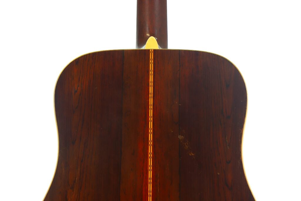 Die Rückseite der Martin D-28 Akustikgitarre aus dem Jahr 1965 mit dunkler Holzoberfläche und einer vertikal in der Mitte verlaufenden Zierintarsie vor einem schlichten weißen Hintergrund. Die Rückseite der Martin D-28 Akustikgitarre aus dem Jahr 1965 mit dunkler Holzoberfläche und einer vertikal in der Mitte verlaufenden Zierintarsie vor einem schlichten weißen Hintergrund.