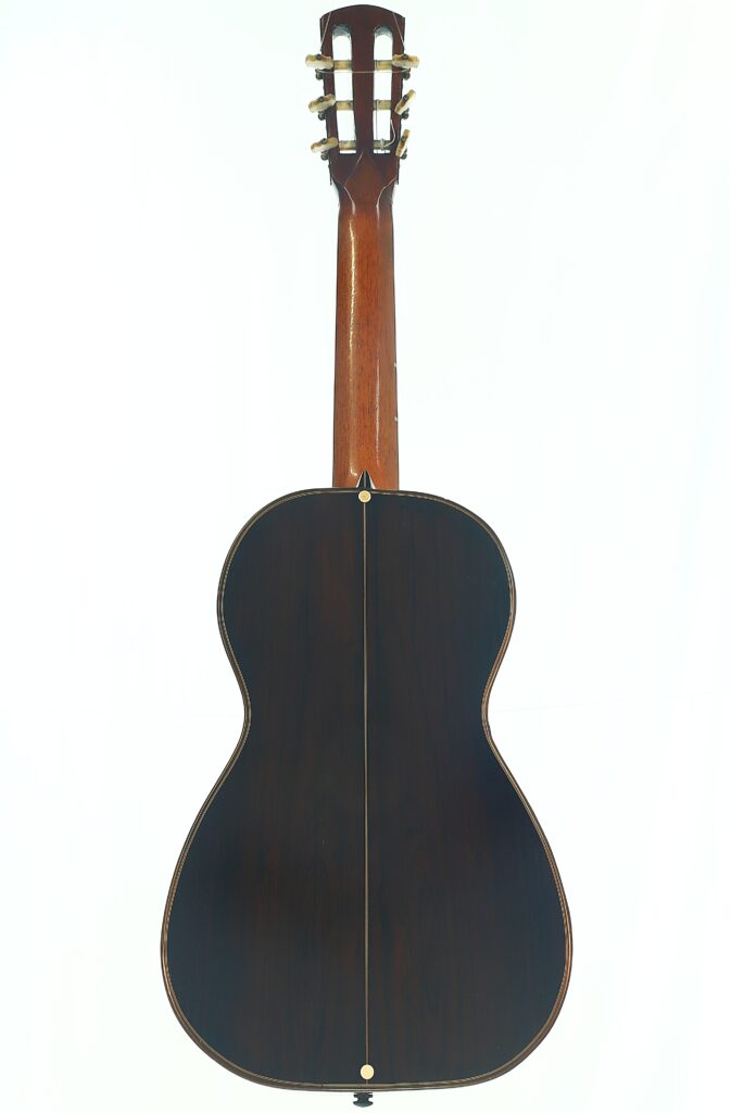 Die Romantikgitarre „Louis Panormo 1827“ wird von hinten gezeigt und präsentiert sich mit ihrer dunklen Holzoberfläche mit einer Mittelnaht sowie einem Holzhals, der mit goldenen Stimmwirbeln versehen ist. Die Romantikgitarre „Louis Panormo 1827“ wird von hinten gezeigt und präsentiert sich mit ihrer dunklen Holzoberfläche mit einer Mittelnaht sowie einem Holzhals, der mit goldenen Stimmwirbeln versehen ist.