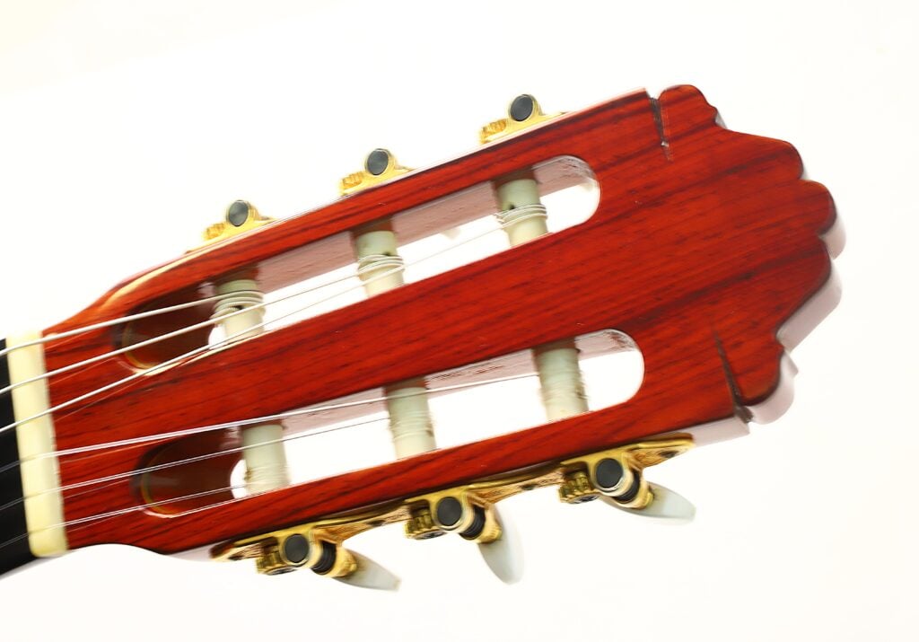 Nahaufnahme des Kopfes einer Paulino Bernabe M-5 2008 Klassische Gitarre mit Stimmwirbeln und Nylonsaiten, polierter Holzmaserung und goldfarbenen Beschlägen vor weißem Hintergrund. Nahaufnahme des Kopfes einer Paulino Bernabe M-5 2008 Klassische Gitarre mit Stimmwirbeln und Nylonsaiten, polierter Holzmaserung und goldfarbenen Beschlägen vor weißem Hintergrund.
