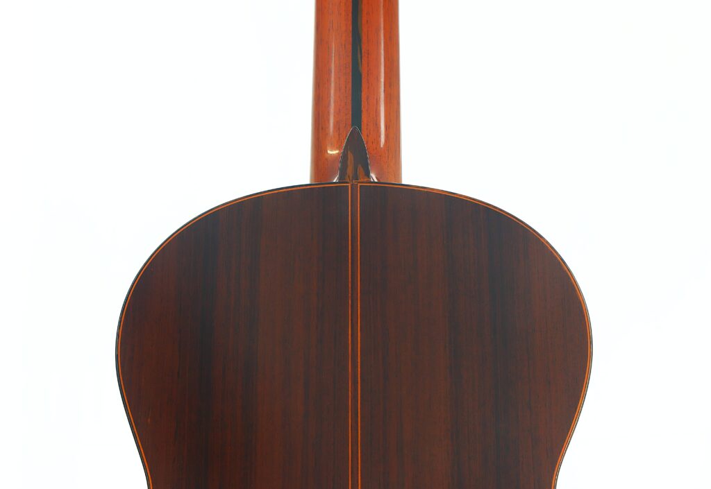 Nahaufnahme der Rückseite einer Ramirez 1a 1985 Klassische Gitarre, die den Holzkorpus und den Hals mit einer Mittellinie sowie feinen Maserungsdetails zeigt. Nahaufnahme der Rückseite einer Ramirez 1a 1985 Klassische Gitarre, die den Holzkorpus und den Hals mit einer Mittellinie sowie feinen Maserungsdetails zeigt.