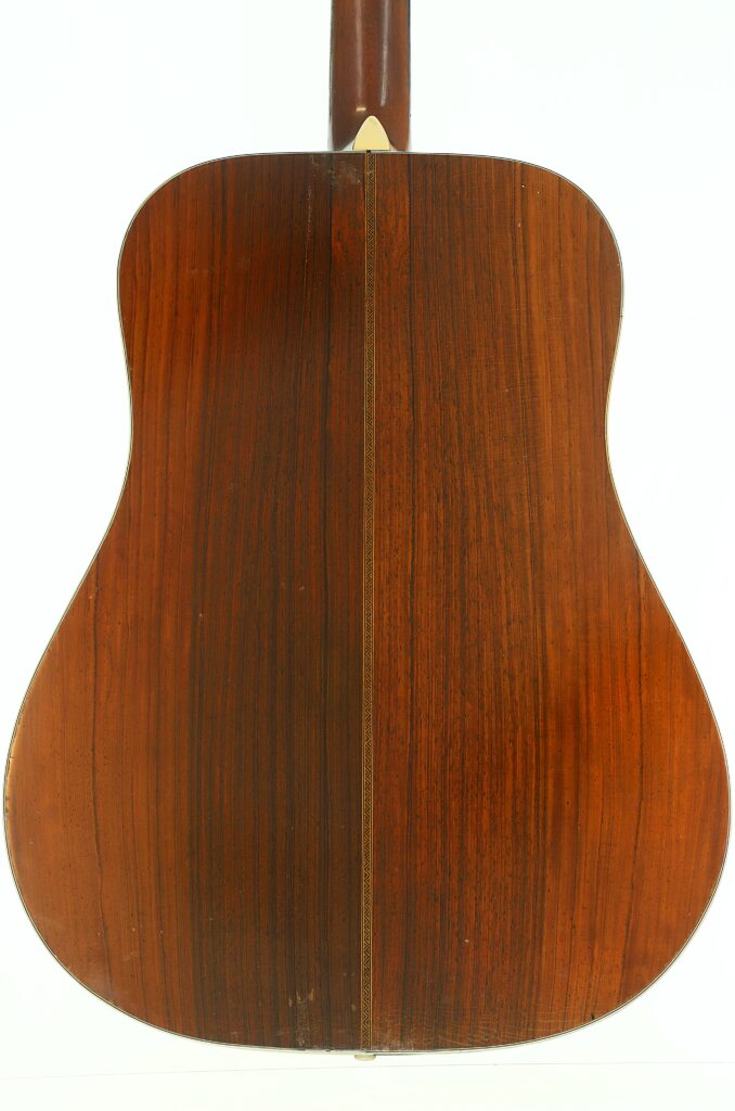 Die Rückseite der Martin D-28 1941 Pre-War Akustikgitarre besticht durch eine satte braune Holzmaserung mit einer vertikalen Naht, die in der Mitte verläuft. Die Rückseite der Martin D-28 1941 Pre-War Akustikgitarre besticht durch eine satte braune Holzmaserung mit einer vertikalen Naht, die in der Mitte verläuft.