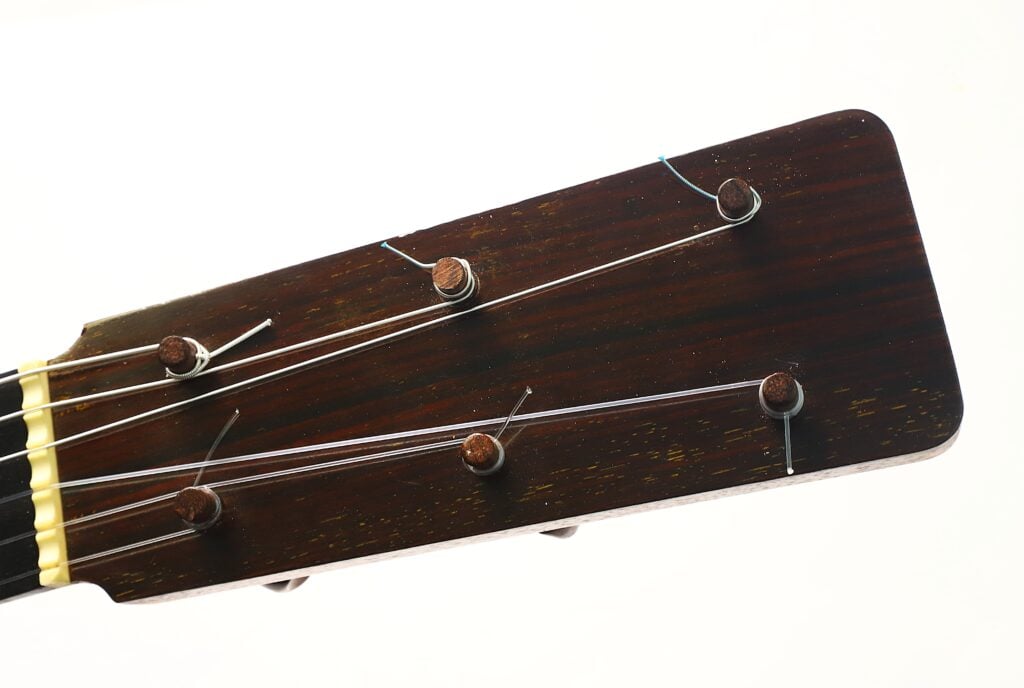 Nahaufnahme des Kopfes der „Antonio Garcia de Lorca 1847 Replika Klassische Gitarre“ mit sechs Stimmwirbeln, einer Holzoberfläche und Metallsaiten vor weißem Hintergrund. Nahaufnahme des Kopfes der „Antonio Garcia de Lorca 1847 Replika Klassische Gitarre“ mit sechs Stimmwirbeln, einer Holzoberfläche und Metallsaiten vor weißem Hintergrund.