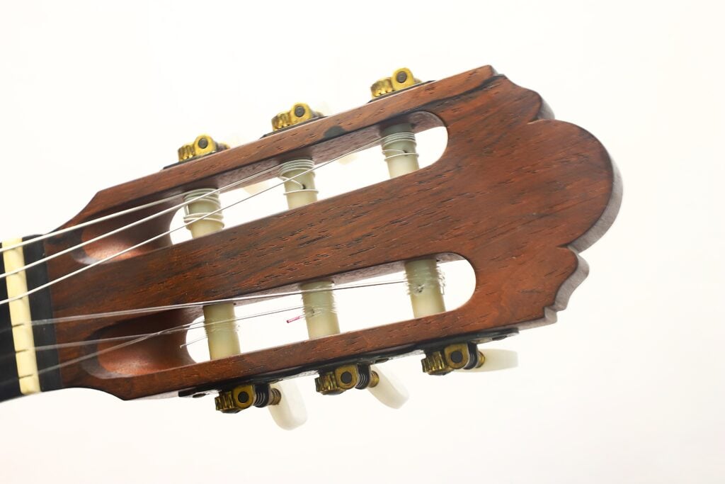 Nahaufnahme des Kopfstücks der „Tosca Klassische Gitarre“ von Frank-Peter Dietrich aus dem Jahr 1998, mit ihren Stimmwirbeln, Saiten und der Holzoberfläche vor einem schlichten weißen Hintergrund. Nahaufnahme des Kopfstücks der „Tosca Klassische Gitarre“ von Frank-Peter Dietrich aus dem Jahr 1998, mit ihren Stimmwirbeln, Saiten und der Holzoberfläche vor einem schlichten weißen Hintergrund.