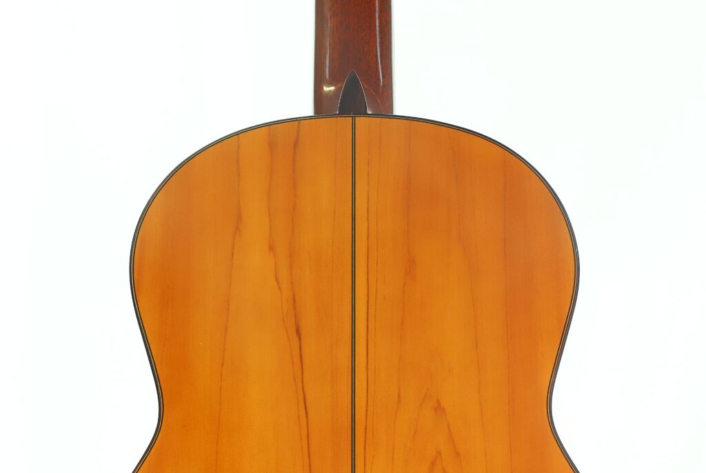 Rückansicht der Flamenco-Gitarre „Casa Arcangel Fernandez 1970“ mit einer glänzenden, hellen Holzoberfläche mit dunkler Mittelnaht und einem Hals aus dunklem Holz, abgebildet vor einem schlichten weißen Hintergrund. Rückansicht der Flamenco-Gitarre „Casa Arcangel Fernandez 1970“ mit einer glänzenden, hellen Holzoberfläche mit dunkler Mittelnaht und einem Hals aus dunklem Holz, abgebildet vor einem schlichten weißen Hintergrund.