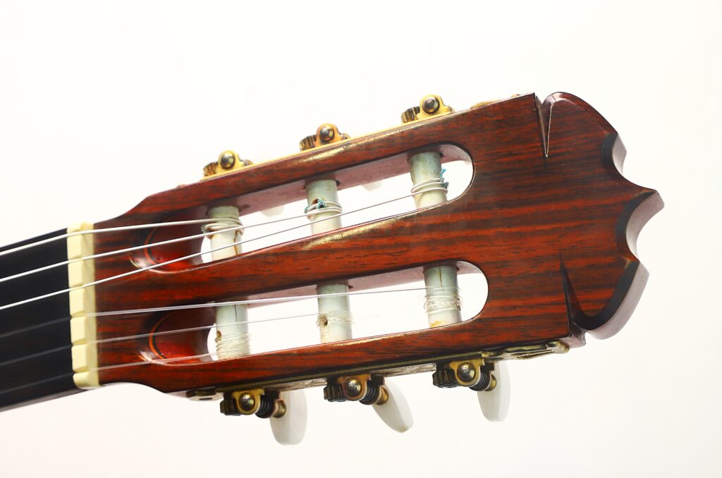 Nahaufnahme des Kopfes einer Ramirez 1a „Klassische Gitarre“ aus dem Jahr 1985 mit Stimmwirbeln, Holzoberfläche und Nylonsaiten vor weißem Hintergrund. Nahaufnahme des Kopfes einer Ramirez 1a „Klassische Gitarre“ aus dem Jahr 1985 mit Stimmwirbeln, Holzoberfläche und Nylonsaiten vor weißem Hintergrund.