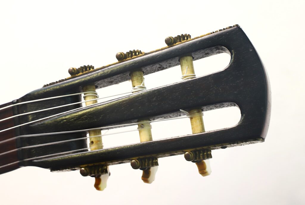 Nahaufnahme des Kopfstücks einer „Romantikgitarre“ von Louis Panormo aus dem Jahr 1827, auf der die Stimmwirbel, die Zahnräder und die Saiten vor weißem Hintergrund zu sehen sind. Nahaufnahme des Kopfstücks einer „Romantikgitarre“ von Louis Panormo aus dem Jahr 1827, auf der die Stimmwirbel, die Zahnräder und die Saiten vor weißem Hintergrund zu sehen sind.