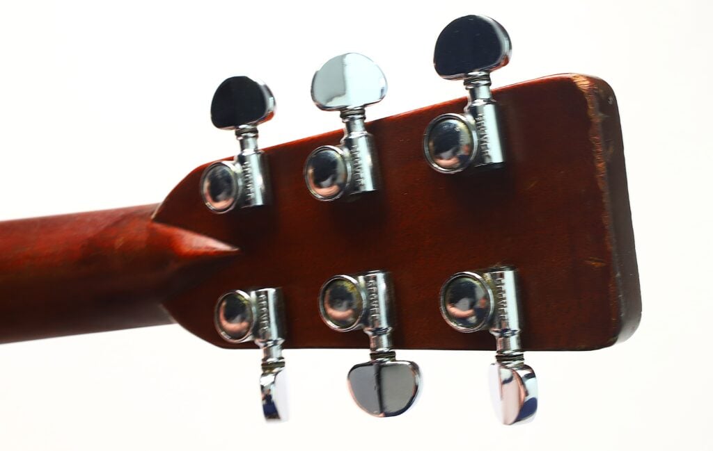 Nahaufnahme der Rückseite des Kopfstücks einer Martin D-28 Akustikgitarre aus dem Jahr 1965, auf der sechs glänzende Chrom-Stimmwirbel an einem Holzhals vor weißem Hintergrund zu sehen sind. Nahaufnahme der Rückseite des Kopfstücks einer Martin D-28 Akustikgitarre aus dem Jahr 1965, auf der sechs glänzende Chrom-Stimmwirbel an einem Holzhals vor weißem Hintergrund zu sehen sind.