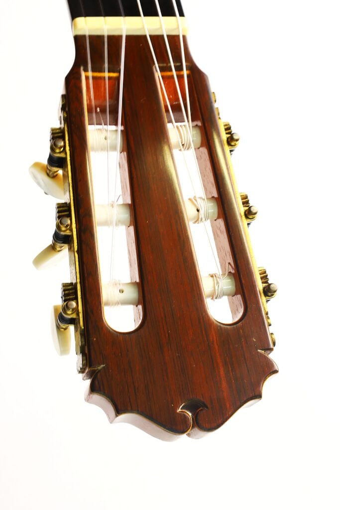 Nahaufnahme des Kopfstücks einer klassischen Gitarre vom Typ „Masaru Kohno Modell 50, Baujahr 1979“ mit Stimmwirbeln und Nylonsaiten, fotografiert vor weißem Hintergrund. Nahaufnahme des Kopfstücks einer klassischen Gitarre vom Typ „Masaru Kohno Modell 50, Baujahr 1979“ mit Stimmwirbeln und Nylonsaiten, fotografiert vor weißem Hintergrund.