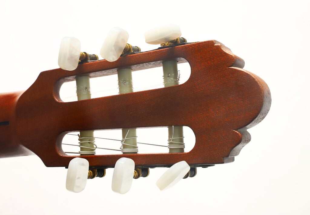 Nahaufnahme des Kopfes der „Tosca Klassische Gitarre“ von Frank-Peter Dietrich aus dem Jahr 1998, auf der die Stimmwirbel, die Saiten und die Holzoberfläche vor einem weißen Hintergrund zu sehen sind. Nahaufnahme des Kopfes der „Tosca Klassische Gitarre“ von Frank-Peter Dietrich aus dem Jahr 1998, auf der die Stimmwirbel, die Saiten und die Holzoberfläche vor einem weißen Hintergrund zu sehen sind.