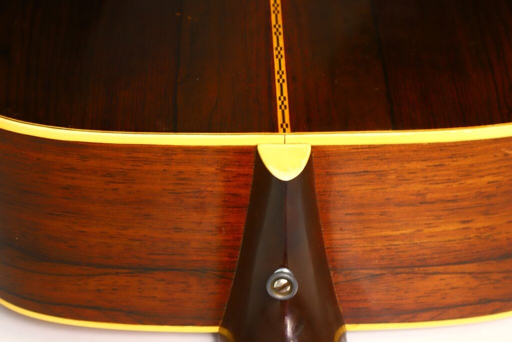Nahaufnahme der Rückseite und der Seite einer Martin D-28 Akustikgitarre aus dem Jahr 1965, bei der die Holzmaserung, die gelbe Einfassung, der dekorative Mittelstreifen und der Halsansatz mit einer sichtbaren Schraube hervorgehoben werden. Nahaufnahme der Rückseite und der Seite einer Martin D-28 Akustikgitarre aus dem Jahr 1965, bei der die Holzmaserung, die gelbe Einfassung, der dekorative Mittelstreifen und der Halsansatz mit einer sichtbaren Schraube hervorgehoben werden.