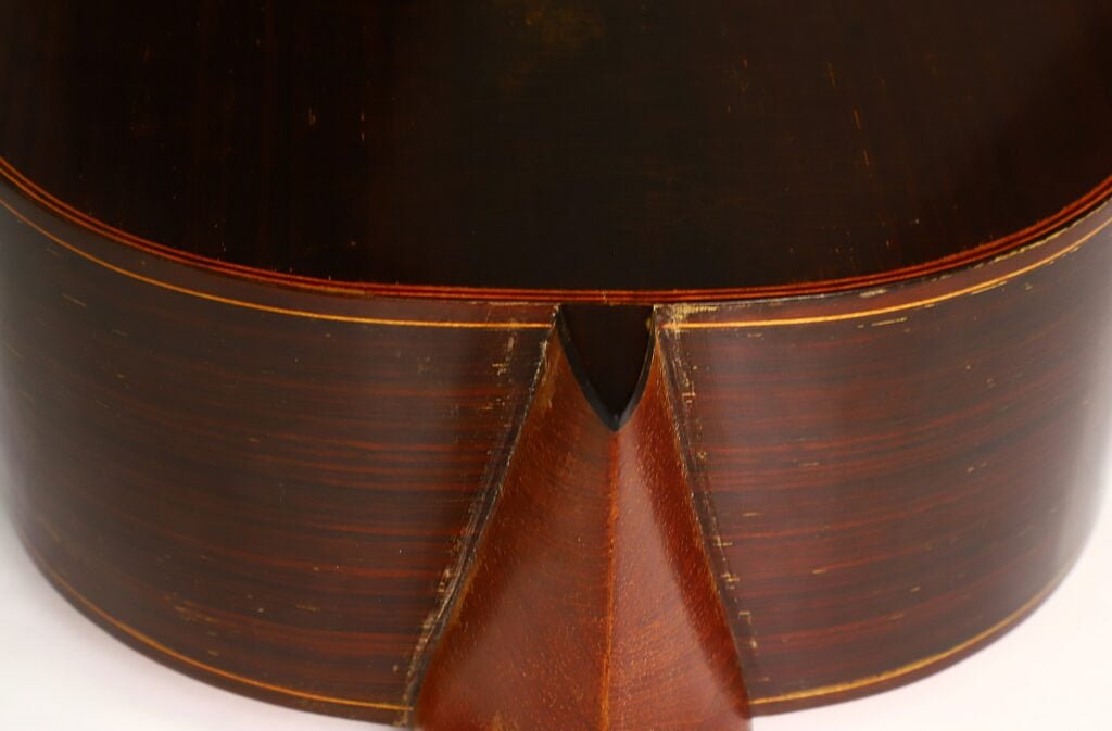 Nahaufnahme der Rückseite und der Unterkante der „Antonio Garcia de Lorca 1847 Replika Klassische Gitarre“, die die Holzmaserung, die Einfassung und ein dekoratives Detail am mittleren Keil hervorhebt. Nahaufnahme der Rückseite und der Unterkante der „Antonio Garcia de Lorca 1847 Replika Klassische Gitarre“, die die Holzmaserung, die Einfassung und ein dekoratives Detail am mittleren Keil hervorhebt.