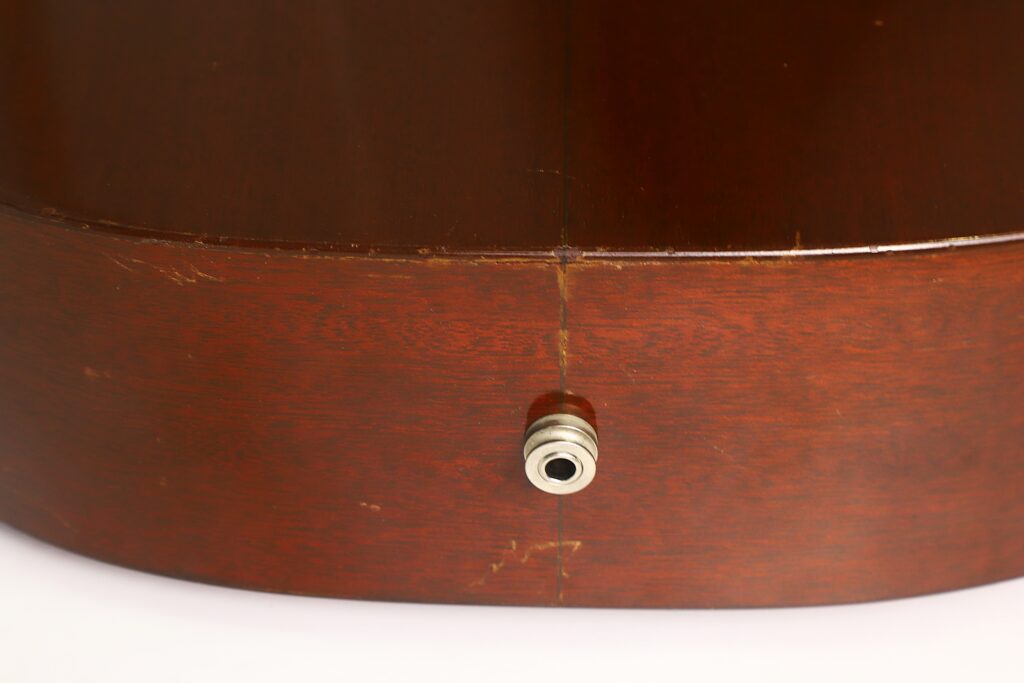 Nahaufnahme der Unterseite des Korpus einer Martin 00-17 Akustikgitarre aus dem Jahr 1941, auf der eine Metall-Ausgangsbuchse zu sehen ist. Das Holz ist glänzend lackiert und weist sichtbare Kratzer sowie eine mittige Naht auf. Nahaufnahme der Unterseite des Korpus einer Martin 00-17 Akustikgitarre aus dem Jahr 1941, auf der eine Metall-Ausgangsbuchse zu sehen ist. Das Holz ist glänzend lackiert und weist sichtbare Kratzer sowie eine mittige Naht auf.