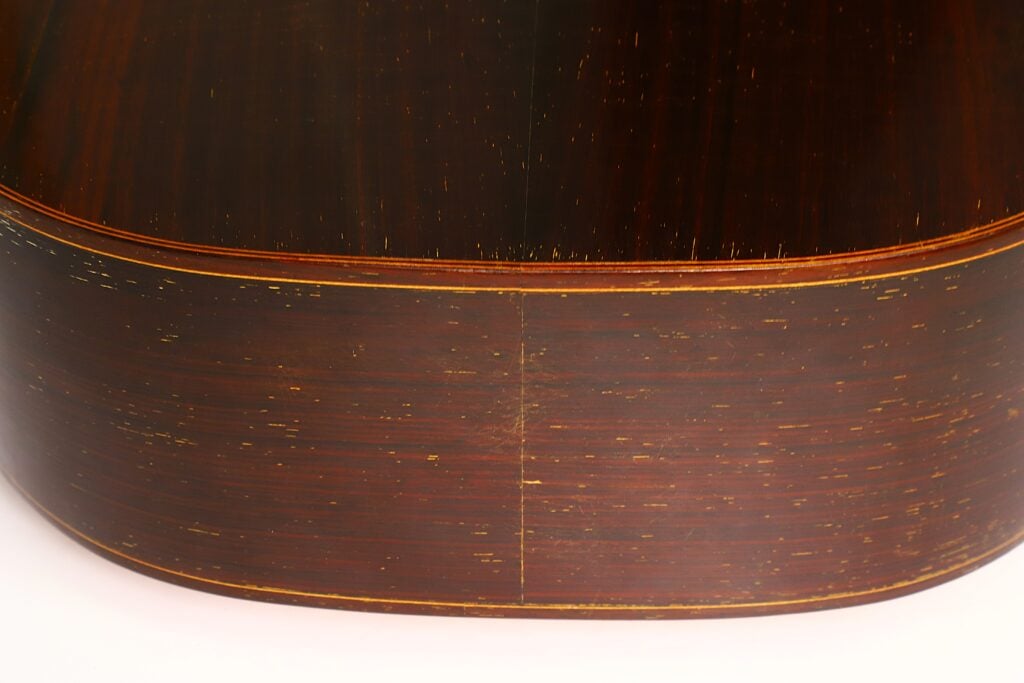 Nahaufnahme der Rückseite und der Seite der „Antonio Garcia de Lorca 1847 Replika Klassische Gitarre“, die die Holzmaserung, eine Mittelnaht und eine glänzende, leicht abgenutzte Lackierung zeigt. Das Bild verdeutlicht die handwerkliche Qualität und die Detailgenauigkeit des Korpus dieser klassischen Gitarre. Nahaufnahme der Rückseite und der Seite der „Antonio Garcia de Lorca 1847 Replika Klassische Gitarre“, die die Holzmaserung, eine Mittelnaht und eine glänzende, leicht abgenutzte Lackierung zeigt. Das Bild verdeutlicht die handwerkliche Qualität und die Detailgenauigkeit des Korpus dieser klassischen Gitarre.