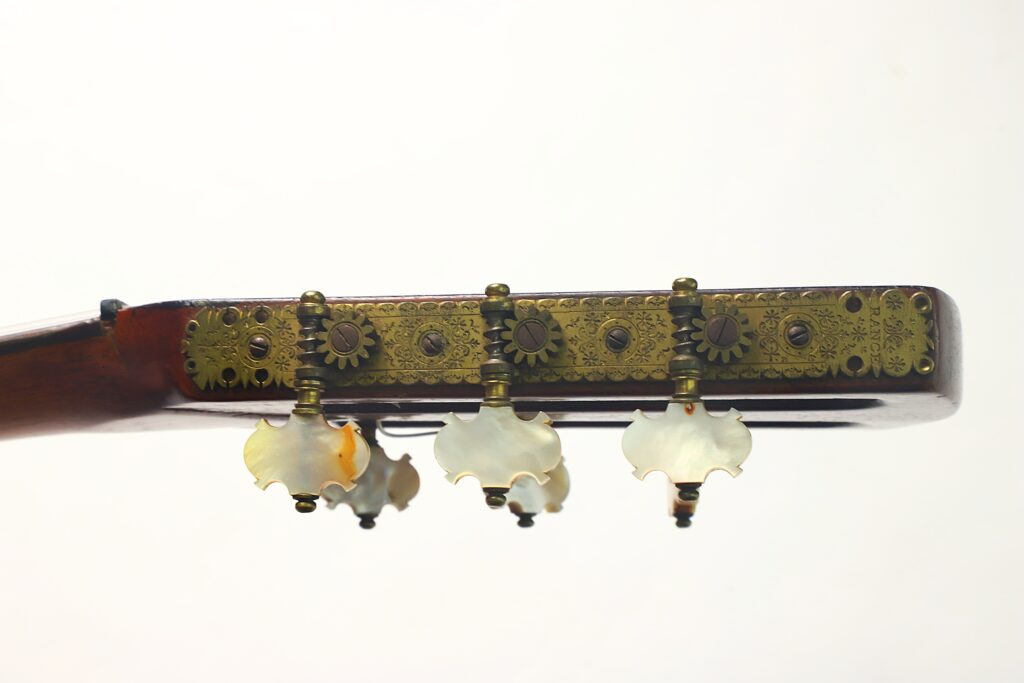 Nahaufnahme der kunstvoll verzierten Stimmwirbel der „Romantikgitarre“ von Louis Panormo aus dem Jahr 1827 mit Perlmutt-Einlagen und aufwendigen Messingverzierungen vor einem schlichten weißen Hintergrund. Nahaufnahme der kunstvoll verzierten Stimmwirbel der „Romantikgitarre“ von Louis Panormo aus dem Jahr 1827 mit Perlmutt-Einlagen und aufwendigen Messingverzierungen vor einem schlichten weißen Hintergrund.
