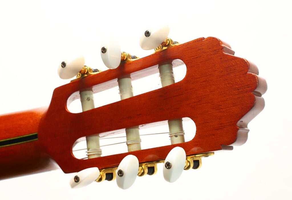 Nahaufnahme des Kopfes und der Stimmwirbel einer Paulino Bernabe M-5 2008 Klassische Gitarre, die drei Nylonsaiten und eine Holzoberfläche vor weißem Hintergrund zeigt. Nahaufnahme des Kopfes und der Stimmwirbel einer Paulino Bernabe M-5 2008 Klassische Gitarre, die drei Nylonsaiten und eine Holzoberfläche vor weißem Hintergrund zeigt.