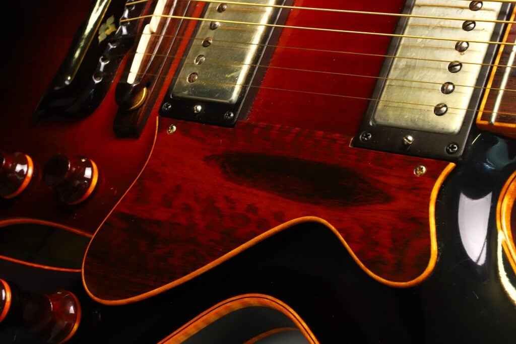 Eine Nahaufnahme der DeLaHaye Elektro-Akustik-Gitarre aus dem Jahr 1995 zeigt ihre Tonabnehmer, Saiten und eine abgenutzte Stelle am Holzkorpus, wodurch die glänzende Lackierung und die feine Holzmaserung besonders gut zur Geltung kommen. Eine Nahaufnahme der DeLaHaye Elektro-Akustik-Gitarre aus dem Jahr 1995 zeigt ihre Tonabnehmer, Saiten und eine abgenutzte Stelle am Holzkorpus, wodurch die glänzende Lackierung und die feine Holzmaserung besonders gut zur Geltung kommen.
