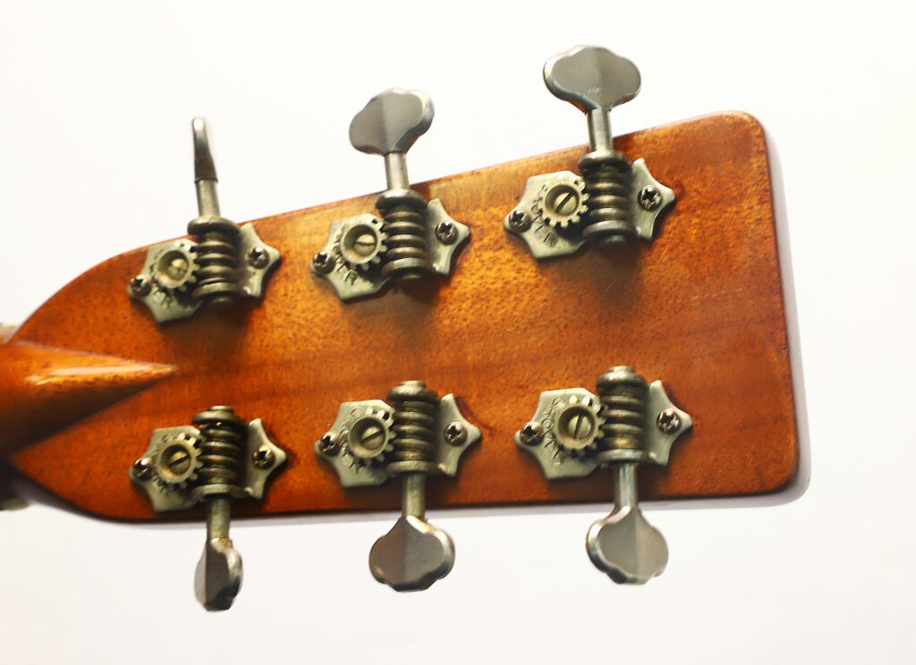 Nahaufnahme der Rückseite des Kopfes einer Martin D-28 1941 Pre-War Akustikgitarre, die sechs Metallstimmwirbel mit Zahnrädern vor weißem Hintergrund zeigt. Nahaufnahme der Rückseite des Kopfes einer Martin D-28 1941 Pre-War Akustikgitarre, die sechs Metallstimmwirbel mit Zahnrädern vor weißem Hintergrund zeigt.