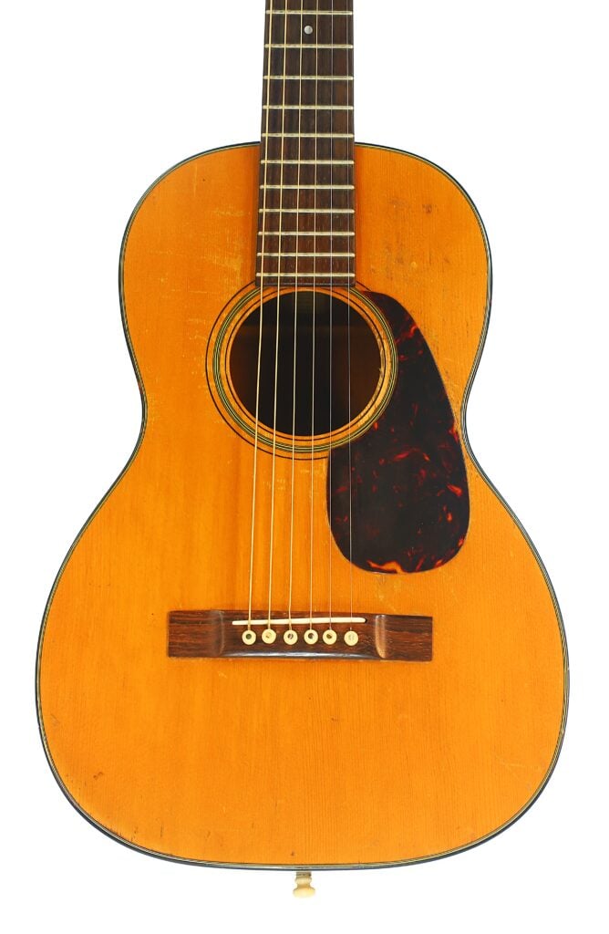 Eine Martin 5-18 Akustikgitarre aus dem Jahr 1958 mit naturbelassener Holzoberfläche, sechs Saiten, dunklem Schlagbrett und sichtbaren Gebrauchsspuren. Das Bild zeigt den Korpus und den Hals. Eine Martin 5-18 Akustikgitarre aus dem Jahr 1958 mit naturbelassener Holzoberfläche, sechs Saiten, dunklem Schlagbrett und sichtbaren Gebrauchsspuren. Das Bild zeigt den Korpus und den Hals.