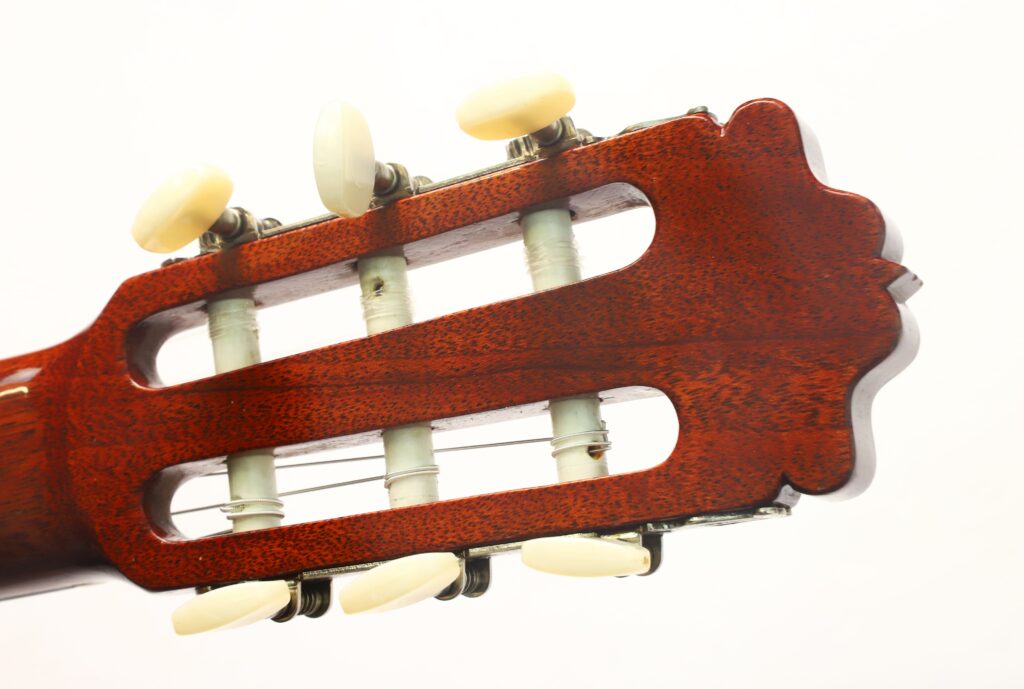 Nahaufnahme des Kopfstücks einer Flamenco-Gitarre von Casa Arcangel Fernandez aus dem Jahr 1970, die vor einem schlichten weißen Hintergrund ihre Holzoberfläche, die weißen Stimmwirbel und einen Teil des Stimmmechanismus zeigt. Nahaufnahme des Kopfstücks einer Flamenco-Gitarre von Casa Arcangel Fernandez aus dem Jahr 1970, die vor einem schlichten weißen Hintergrund ihre Holzoberfläche, die weißen Stimmwirbel und einen Teil des Stimmmechanismus zeigt.