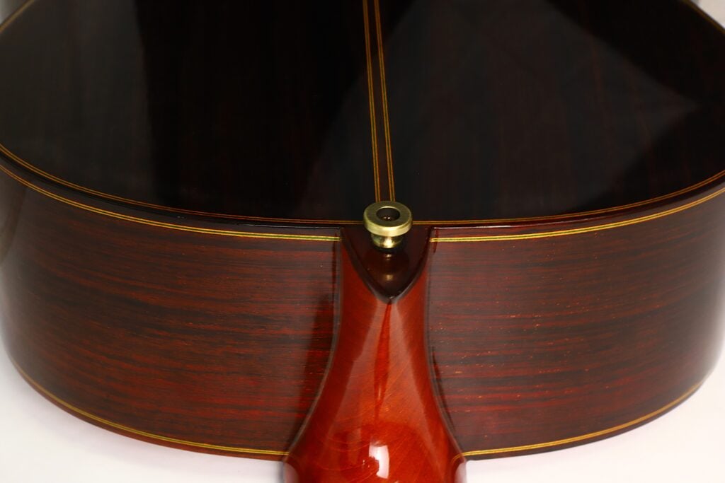 Nahaufnahme des Hals-Korpus-Übergangs der Paulino Bernabe M-5 2008 Klassische Gitarre, die die glänzende, dunkle Holzoberfläche, die feine Maserung und die Zierintarsien entlang der Korpus-Hals-Naht hervorhebt. Nahaufnahme des Hals-Korpus-Übergangs der Paulino Bernabe M-5 2008 Klassische Gitarre, die die glänzende, dunkle Holzoberfläche, die feine Maserung und die Zierintarsien entlang der Korpus-Hals-Naht hervorhebt.