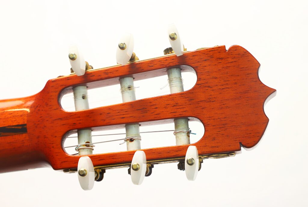 Nahaufnahme des Kopfes einer Ramirez 1a „Klassische Gitarre“ aus dem Jahr 1985, die die Stimmwirbel, die Saiten und die Holzmaserung vor einem schlichten weißen Hintergrund zeigt. Nahaufnahme des Kopfes einer Ramirez 1a „Klassische Gitarre“ aus dem Jahr 1985, die die Stimmwirbel, die Saiten und die Holzmaserung vor einem schlichten weißen Hintergrund zeigt.