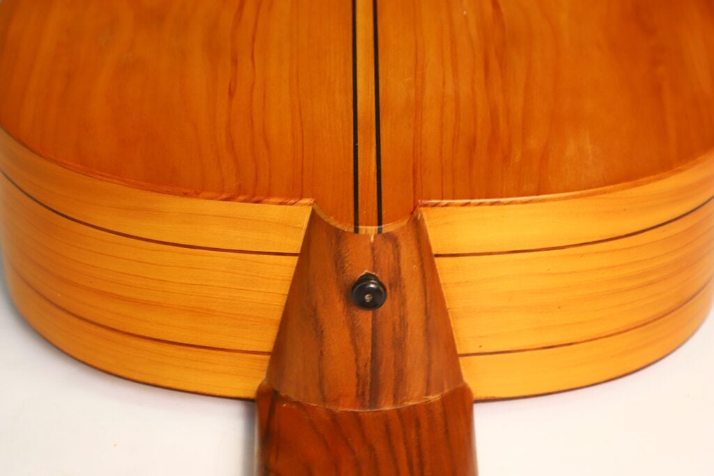 Nahaufnahme des Holzrückens der Hans Herb Vihuela von 1989 mit Fokus auf die Verbindung zwischen Korpus und Hals, die die Maserung des Holzes und den Gurtknopf zeigt. Nahaufnahme des Holzrückens der Hans Herb Vihuela von 1989 mit Fokus auf die Verbindung zwischen Korpus und Hals, die die Maserung des Holzes und den Gurtknopf zeigt.