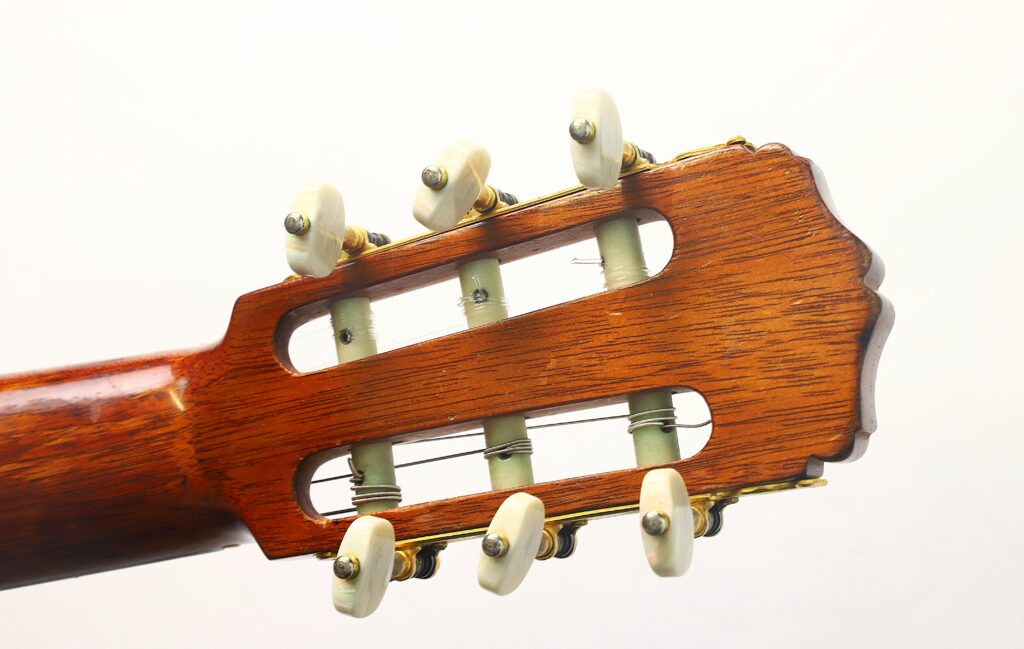 Nahaufnahme des Kopfes der Francisco-Barba-Flamenco-Gitarre von 1966 mit Holzoberfläche, drei Stimmwirbeln auf jeder Seite und Nylonsaiten vor weißem Hintergrund. Nahaufnahme des Kopfes der Francisco-Barba-Flamenco-Gitarre von 1966 mit Holzoberfläche, drei Stimmwirbeln auf jeder Seite und Nylonsaiten vor weißem Hintergrund.