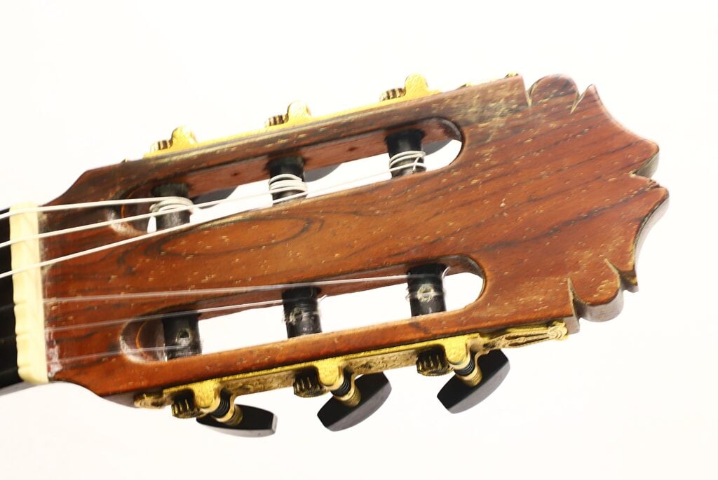 Nahaufnahme des Kopfes der „Andres Martin 1966 Klassische Gitarre“ mit Stimmwirbeln aus Holz, Metallsaiten und goldfarbenen Mechaniken vor weißem Hintergrund. Nahaufnahme des Kopfes der „Andres Martin 1966 Klassische Gitarre“ mit Stimmwirbeln aus Holz, Metallsaiten und goldfarbenen Mechaniken vor weißem Hintergrund.