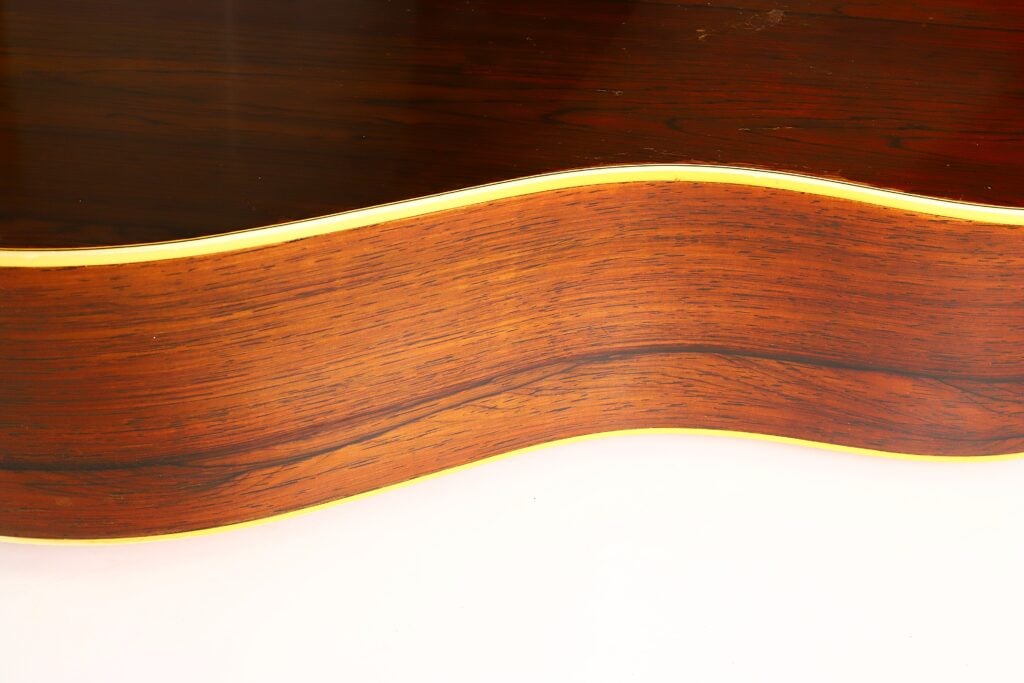 Nahaufnahme der Holzseite einer Martin D-28 Akustikgitarre aus dem Jahr 1965, die die charakteristische Maserung und die hellen Zierleisten vor weißem Hintergrund hervorhebt. Nahaufnahme der Holzseite einer Martin D-28 Akustikgitarre aus dem Jahr 1965, die die charakteristische Maserung und die hellen Zierleisten vor weißem Hintergrund hervorhebt.