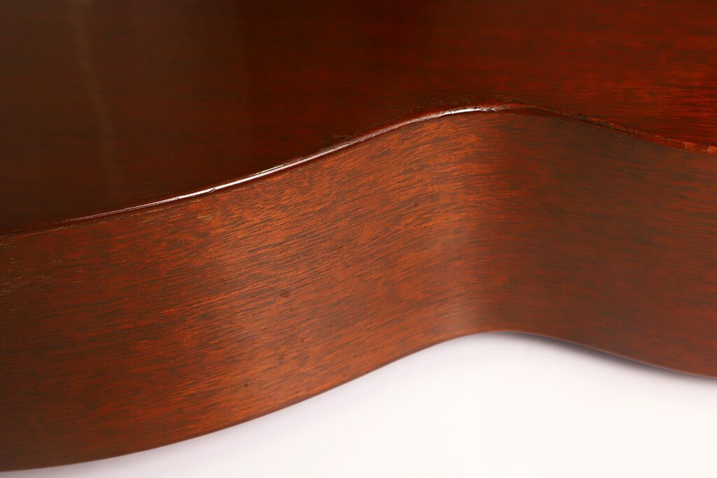 Nahaufnahme des polierten Korpus einer Martin 00-17 Akustikgitarre aus dem Jahr 1941, bei der die geschwungene Kante und die glatte, sattbraune Holzmaserung vor weißem Hintergrund besonders gut zur Geltung kommen. Nahaufnahme des polierten Korpus einer Martin 00-17 Akustikgitarre aus dem Jahr 1941, bei der die geschwungene Kante und die glatte, sattbraune Holzmaserung vor weißem Hintergrund besonders gut zur Geltung kommen.