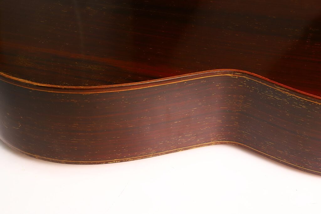 Nahaufnahme der Seite der „Antonio Garcia de Lorca 1847 Replika Klassische Gitarre“, die die Maserung des Holzes und die elegante, geschwungene Form vor einem weißen Hintergrund hervorhebt. Nahaufnahme der Seite der „Antonio Garcia de Lorca 1847 Replika Klassische Gitarre“, die die Maserung des Holzes und die elegante, geschwungene Form vor einem weißen Hintergrund hervorhebt.