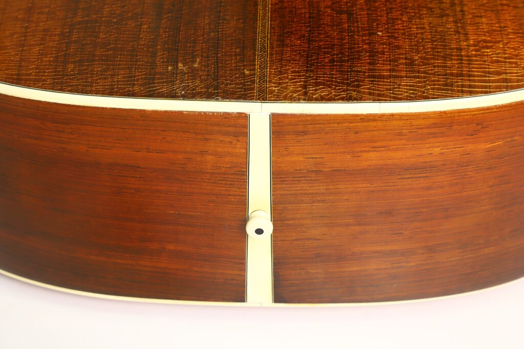 Nahaufnahme der Unterseite der Martin D-28 1941 Pre-War Akustikgitarre, die die Holzmaserung, die cremefarbene Einfassung und einen mittig angeordneten Gurtknopf hervorhebt. Nahaufnahme der Unterseite der Martin D-28 1941 Pre-War Akustikgitarre, die die Holzmaserung, die cremefarbene Einfassung und einen mittig angeordneten Gurtknopf hervorhebt.
