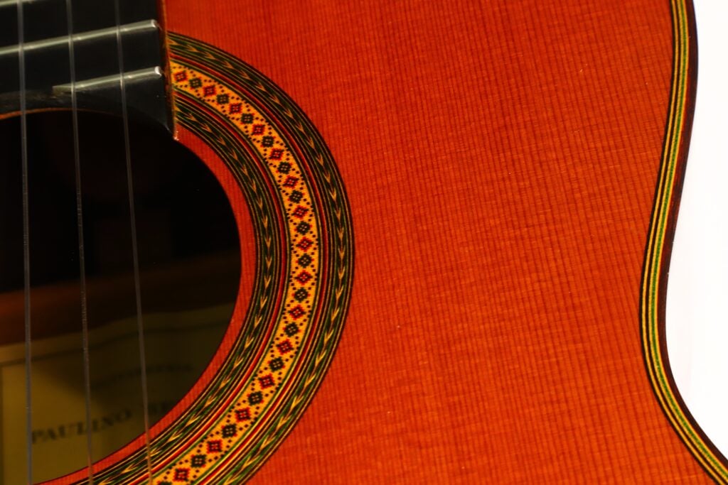 Nahaufnahme des Korpus einer Paulino Bernabe M-5 2008 Klassische Gitarre, die die filigranen Ziermuster rund um das Schallloch und die warme, orange-braune Holzmaserung hervorhebt. Nahaufnahme des Korpus einer Paulino Bernabe M-5 2008 Klassische Gitarre, die die filigranen Ziermuster rund um das Schallloch und die warme, orange-braune Holzmaserung hervorhebt.